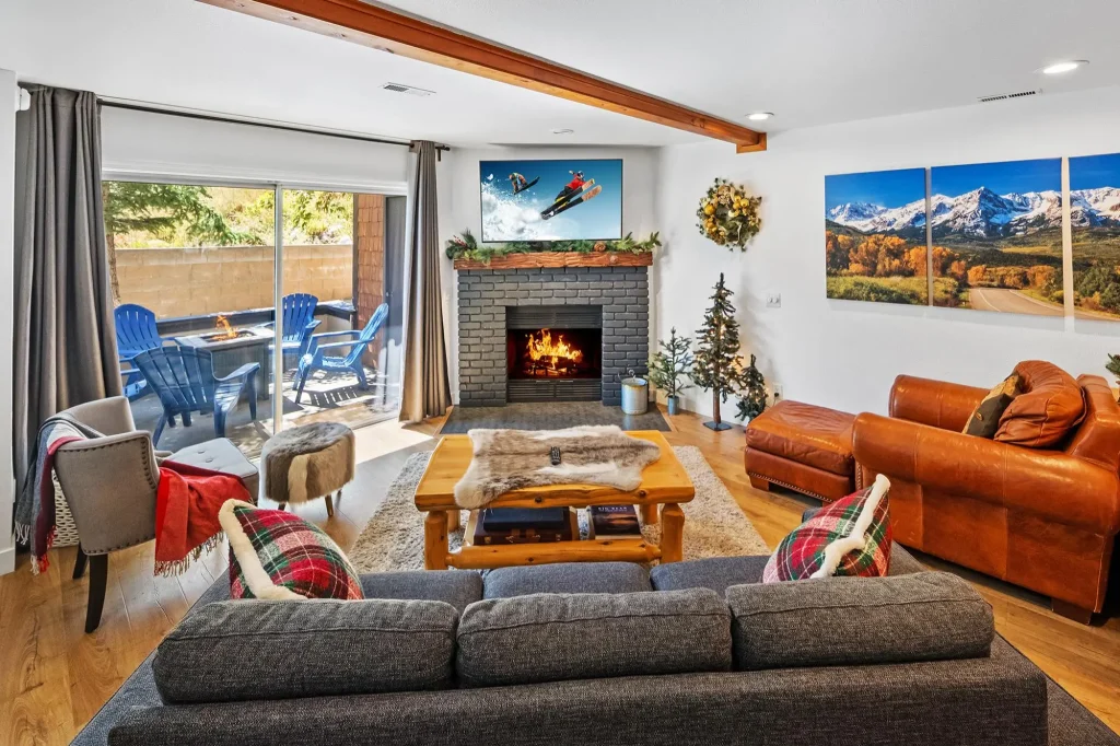 A modern cabin living room in Big Bear with a brick fireplace, gray and leather sofas, and a sliding glass door leading to a patio.