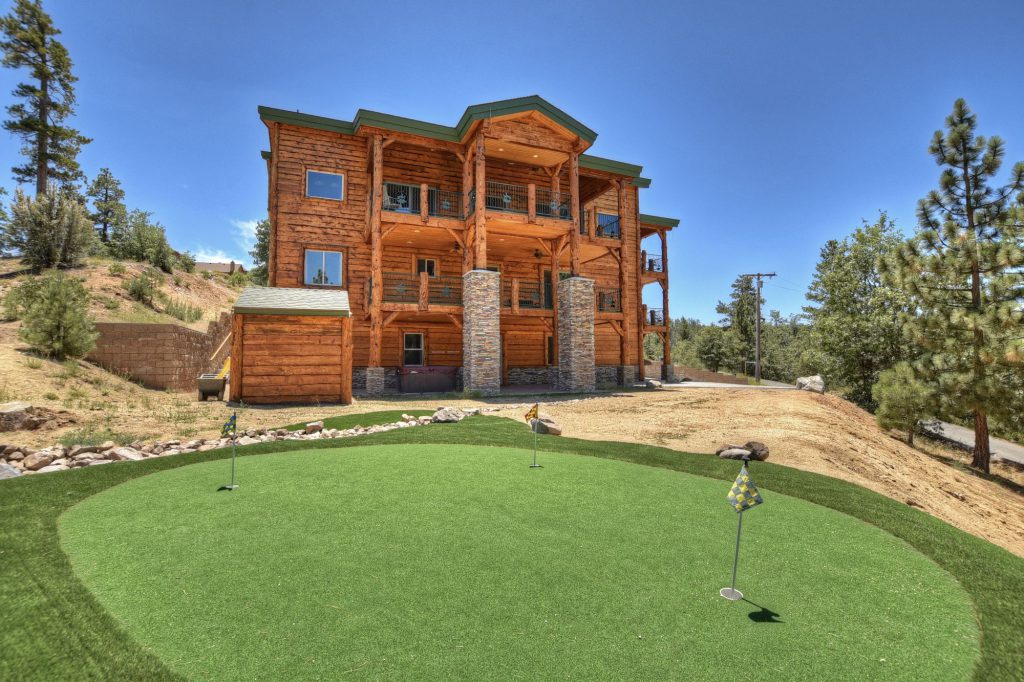 A large, multistory cabin made of wood and stone stands on a hill overlooking a small putting green in the foreground in Big Bear.