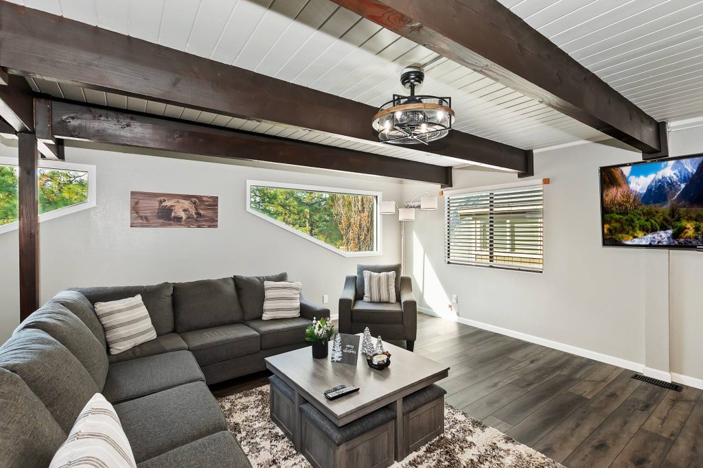 A modern cabin living room in Big Bear with a gray sectional sofa, unique slanted windows, and a ceiling with exposed wooden beams.