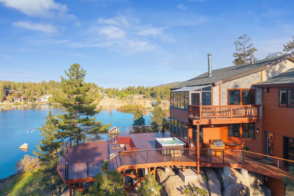 Lakefront cabin at Boulder Bay featuring a spacious deck, hot tub, and scenic lake views surrounded by pine trees.