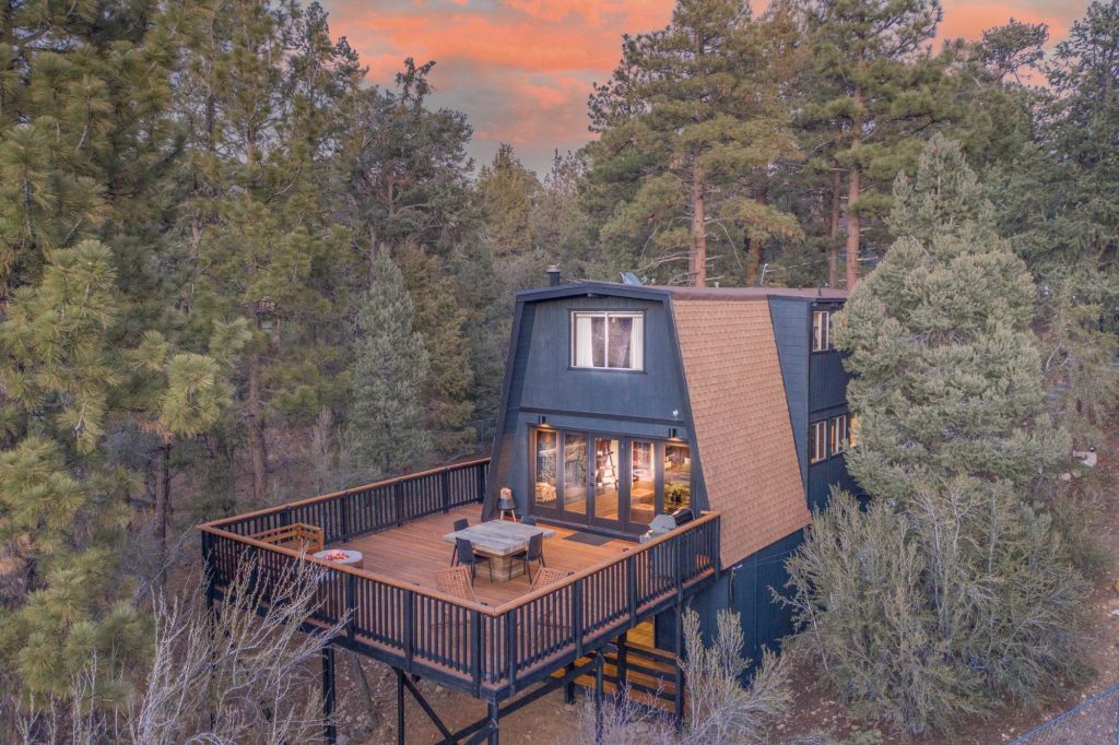 Big Bear Retreat cabin surrounded by pine trees with a spacious elevated deck at sunset