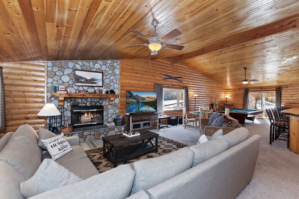 Stork and Bear Cabin living room with stone fireplace, wood walls, comfortable seating, TV, and pool table