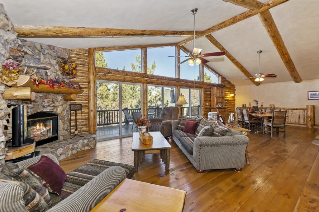 Castle Glen Gem living room with stone fireplace, log walls, large windows, comfortable seating, and dining area