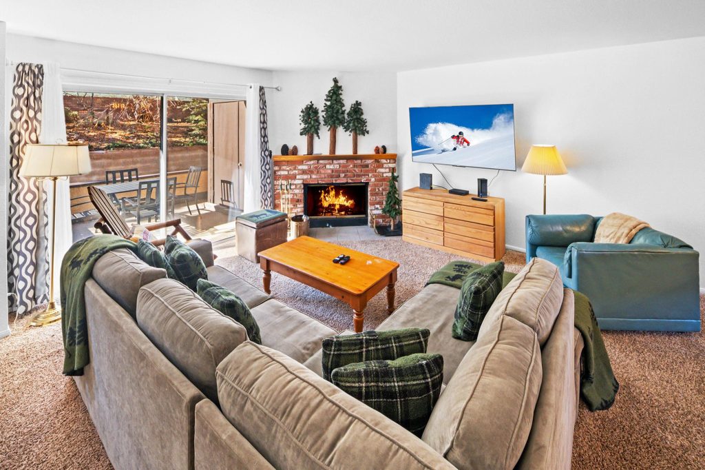 Slopeside Chalet living room with brick fireplace, comfortable sectional seating, TV, and outdoor deck access
