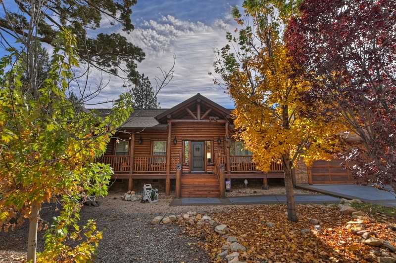 A beautiful, single-story log cabin with a deck and stairs leading to the front door is nestled among colorful autumn trees in Big Bear.