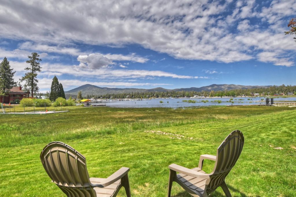 Scenic view from Big Bear Casa showing grassy lawn, outdoor chairs, Big Bear Lake, and surrounding mountains