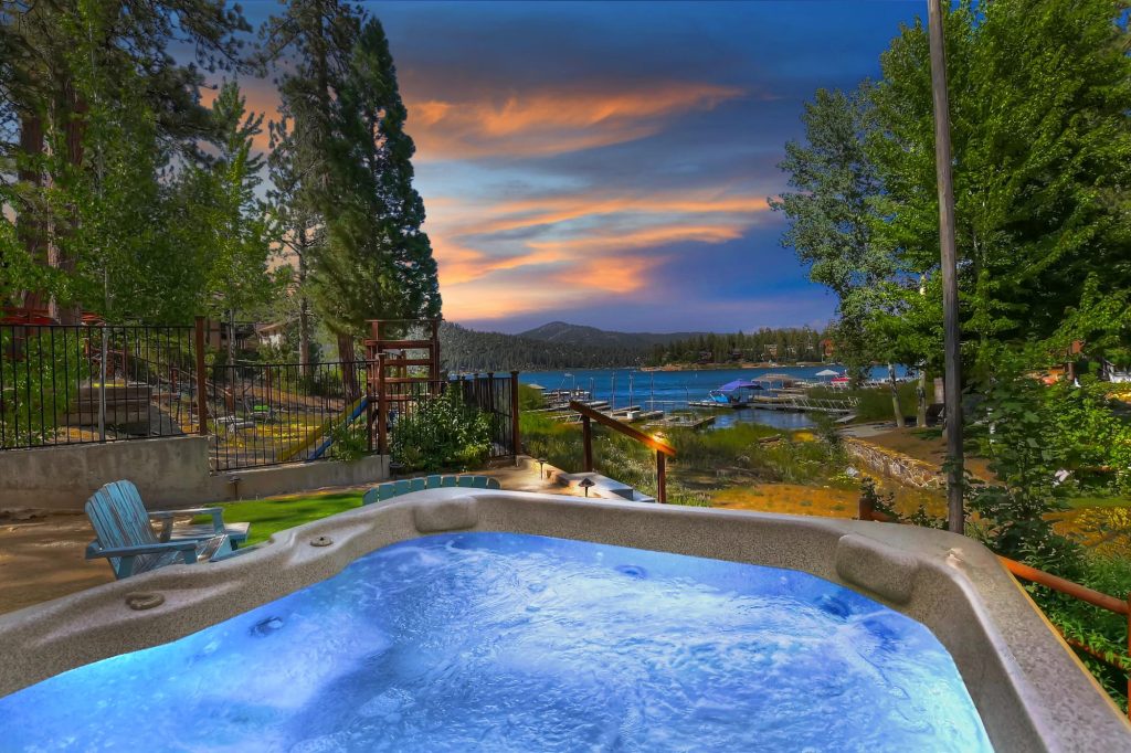 Outdoor hot tub overlooking Big Bear Lake at Papoose Shores with mountain views, trees, and a beautiful sunset sky in Big Bear Lake, CA