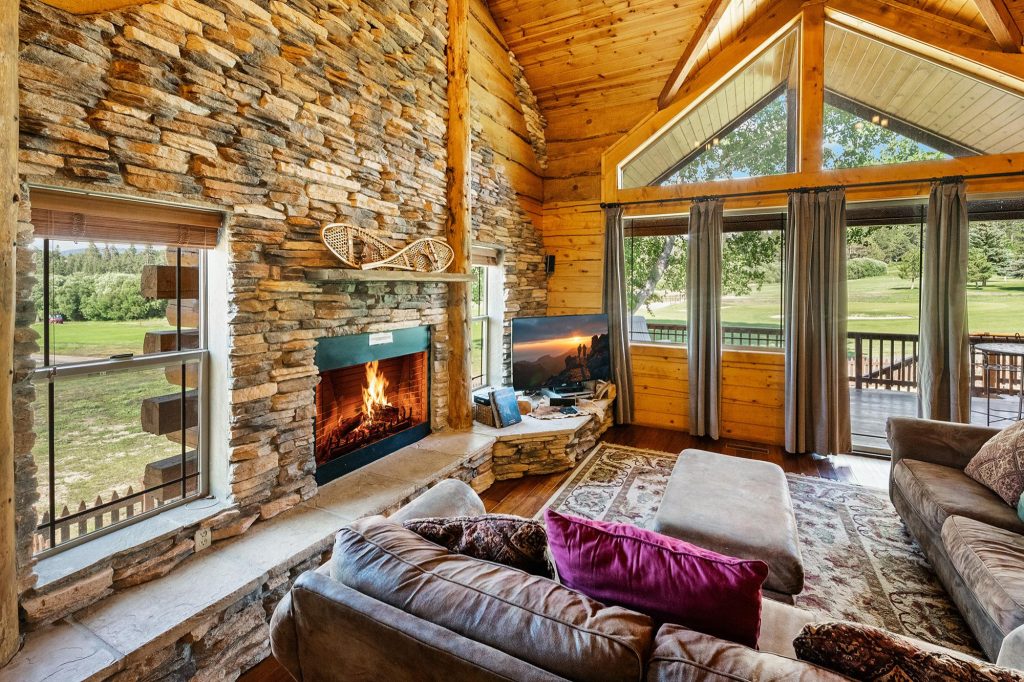 Cozy living room at Retreat at Bear Mountain with stone fireplace, wood interiors, large windows, and forest views in Big Bear Lake, CA