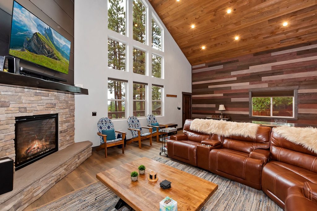 Cozy living room at Ridgecrest Retreat featuring a stone fireplace, leather sectional sofa, and large windows.