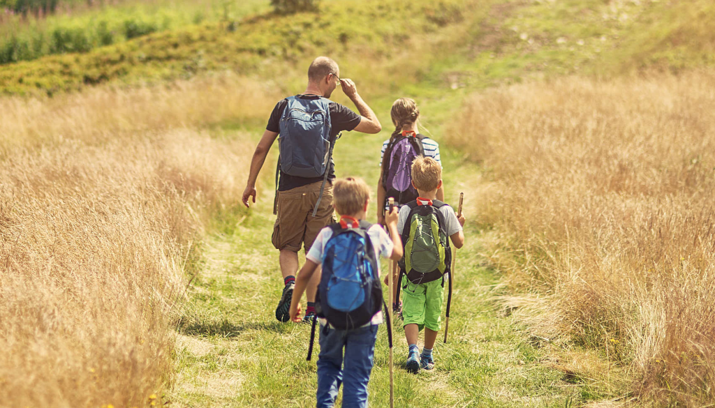 A family of four hikes along a narrow path through a golden grassy meadow in Big Bear.