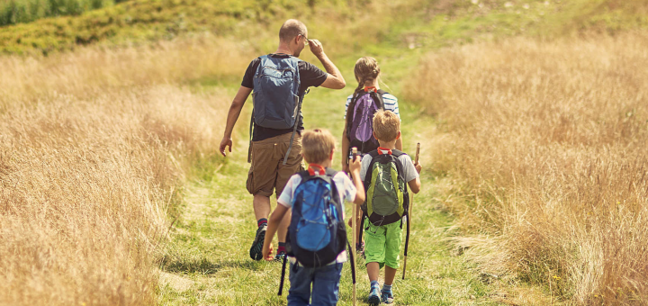 A family of four hikes along a narrow path through a golden grassy meadow in Big Bear.