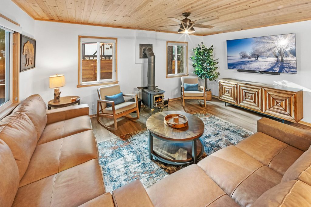 Spacious living room featuring a wooden ceiling, leather sectional sofa, armchairs, coffee table, and large flat-screen TV.