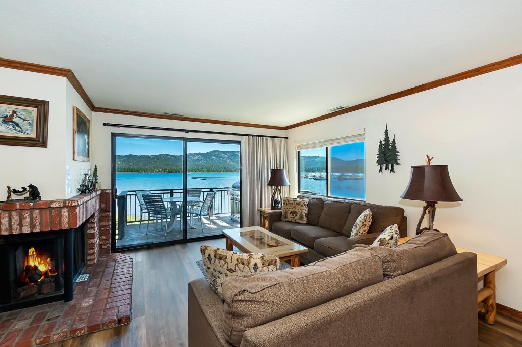 Cozy lakefront cabin living room with fireplace, comfortable seating, and scenic lake views through large windows.