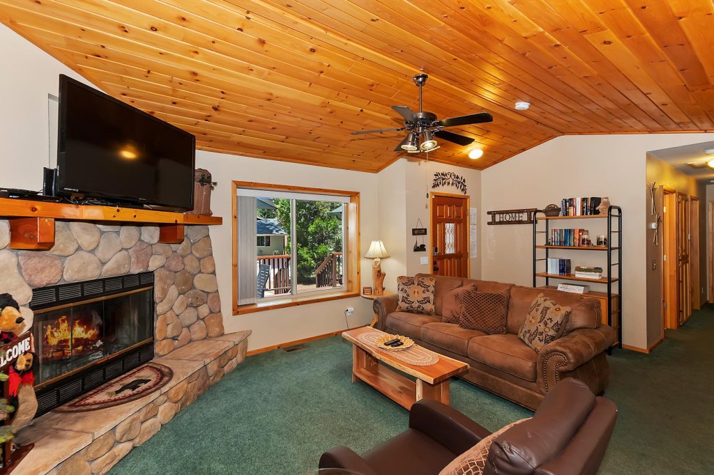 Cozy Freddy's Lake House living room with stone fireplace, wooden ceiling, sofa seating, and rustic cabin decor.