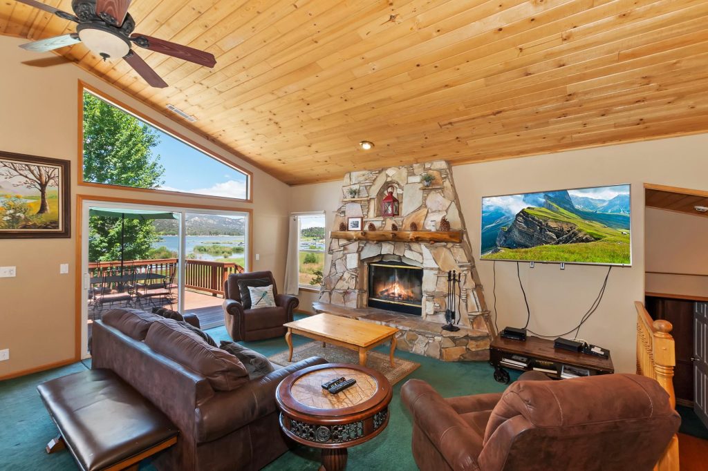 Spacious Lakefront Manor living room with stone fireplace, comfortable seating, large windows, and lake views