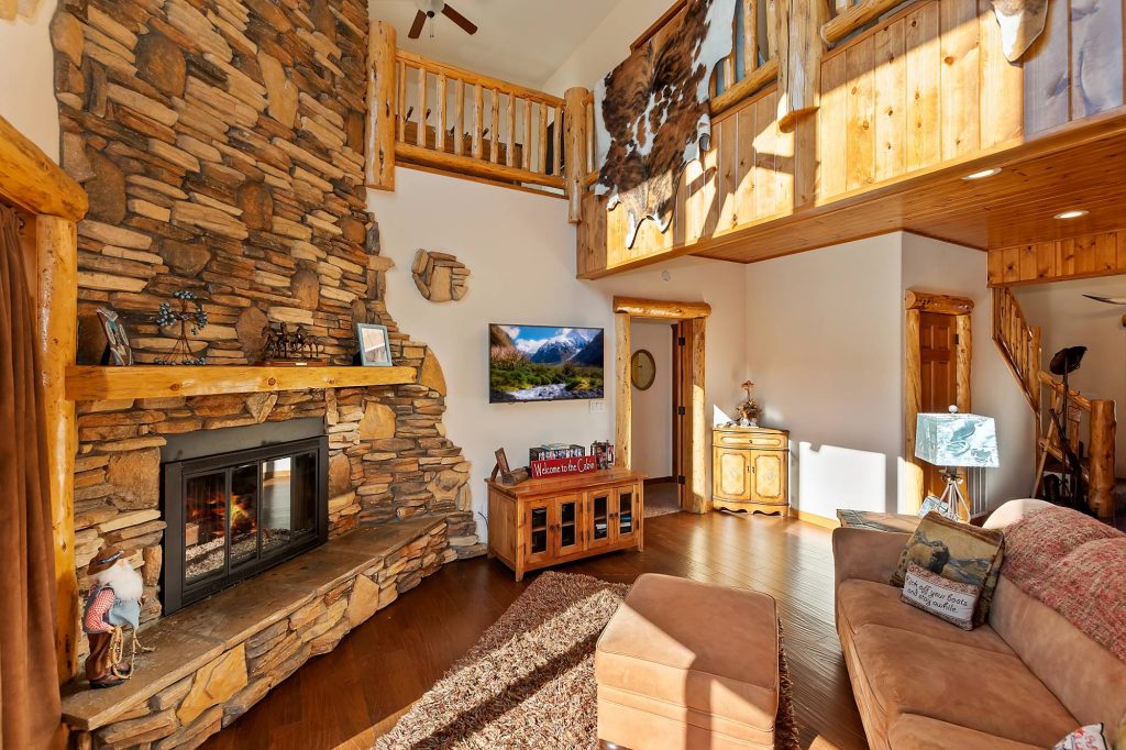 Cozy Longhorn Lodge living room with stone fireplace, wood accents, loft area, and rustic cabin design
