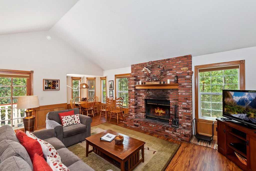 Big Tree Lodge living room with brick fireplace, comfortable seating, dining area, TV, and wood flooring