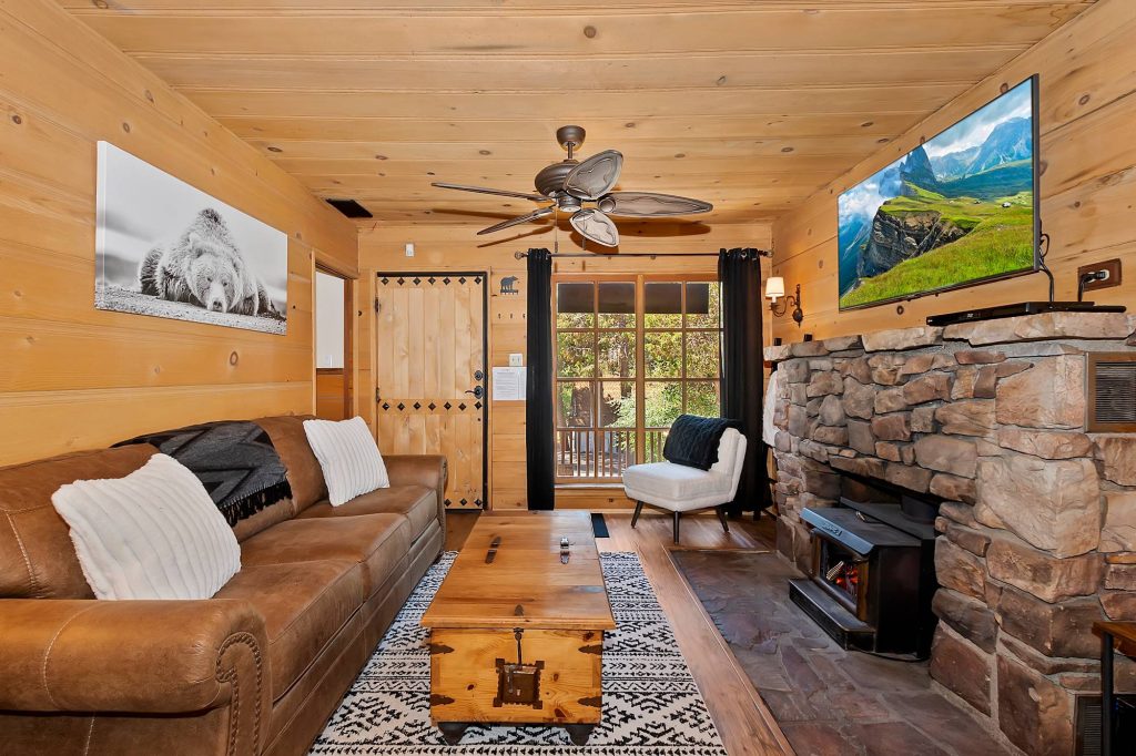 Knotty by Nature cabin interior with stone fireplace, wood walls, sofa, and cozy living area