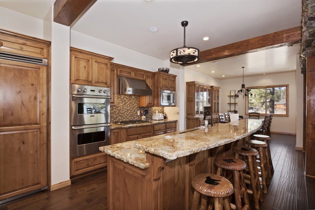 A modern rustic kitchen with light wood cabinets, granite countertops, stainless steel appliances, and a large island with three wooden bar stools in Big Bear.