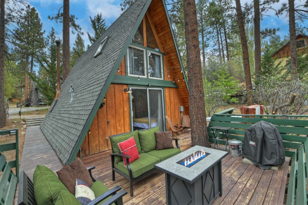 A-frame cabin exterior with outdoor seating area, fire table, and forest surroundings