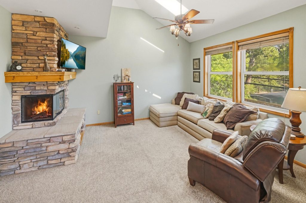 Monterey Manor cabin living room with stone fireplace, comfortable seating, and forest views through windows