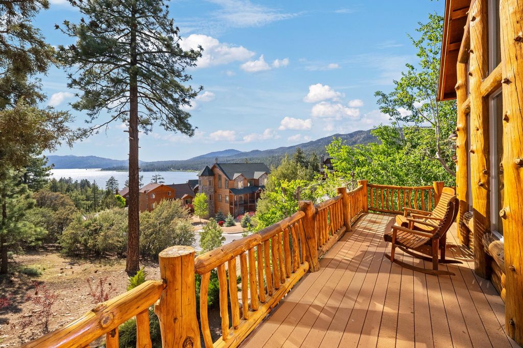 Scenic view from Golden Eagle Lodge in Big Bear featuring a rustic wooden deck, rocking chairs, lake views, and surrounding mountain homes.