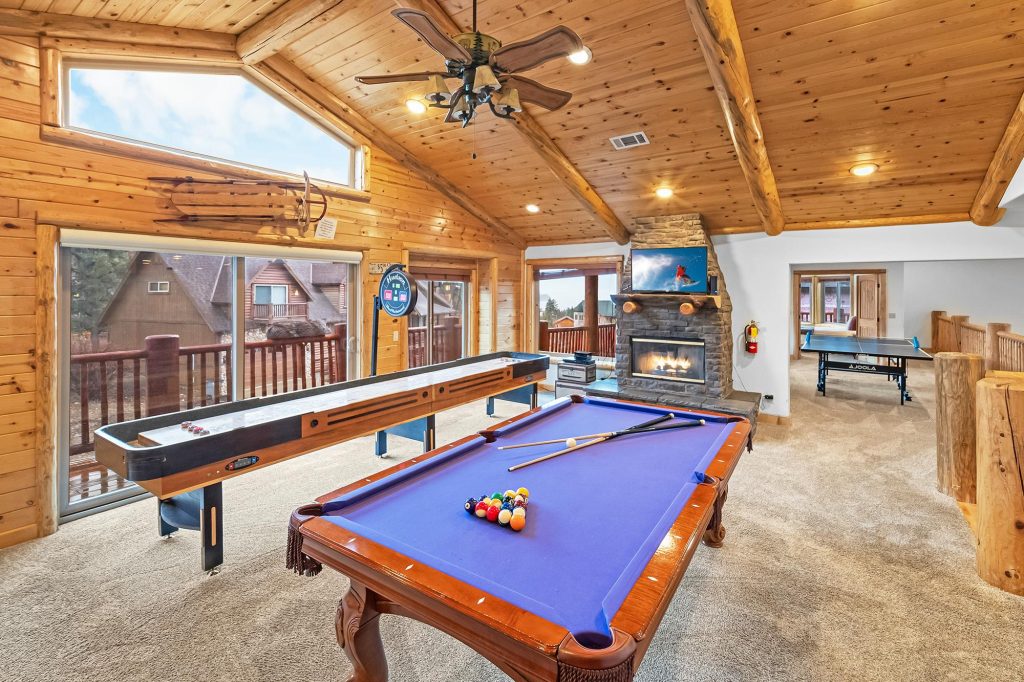 Game room at Eagle Ridge in Big Bear featuring a pool table, shuffleboard, stone fireplace, table tennis area, and large windows with mountain views.