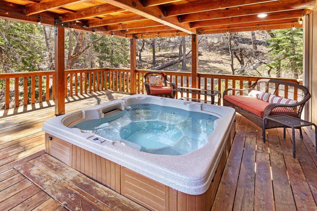 Outdoor hot tub on a wooden deck at Mountain Pines Lodge surrounded by forest views and comfortable seating
