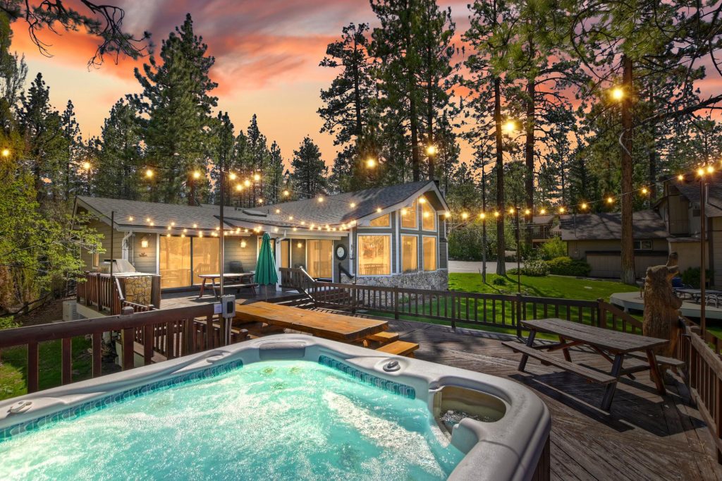 Rear view of a lakefront house with deck, string lights, and backyard seating at sunset.