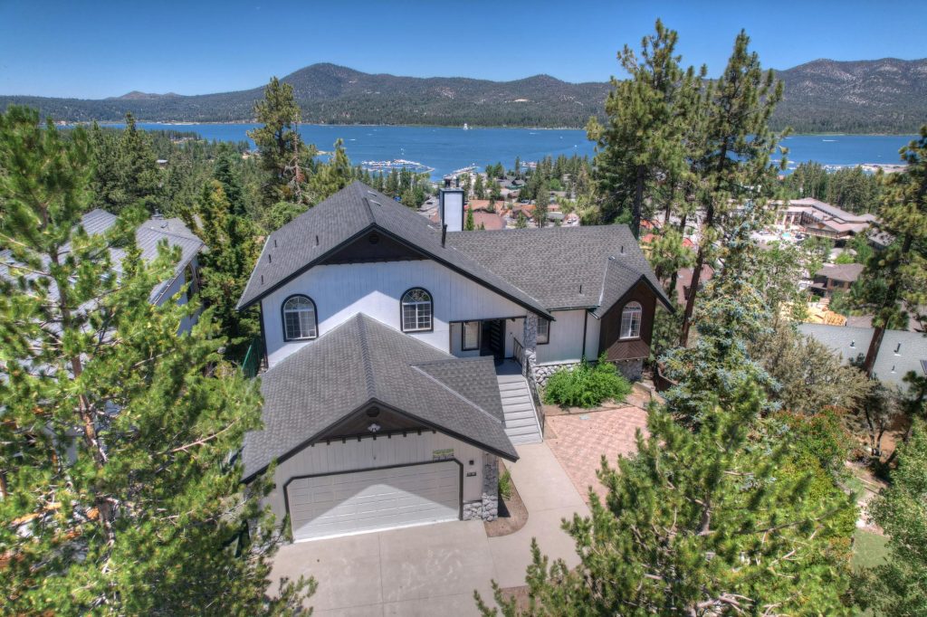 Exterior view of a house with roof and driveway, surrounded by pine trees, overlooking Big Bear Lake.