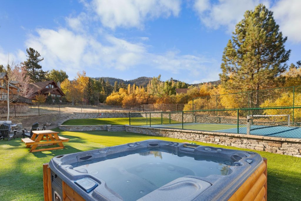 Outdoor hot tub at Geronimo Lodge surrounded by green lawn, mountain views, trees, and a peaceful Big Bear retreat setting