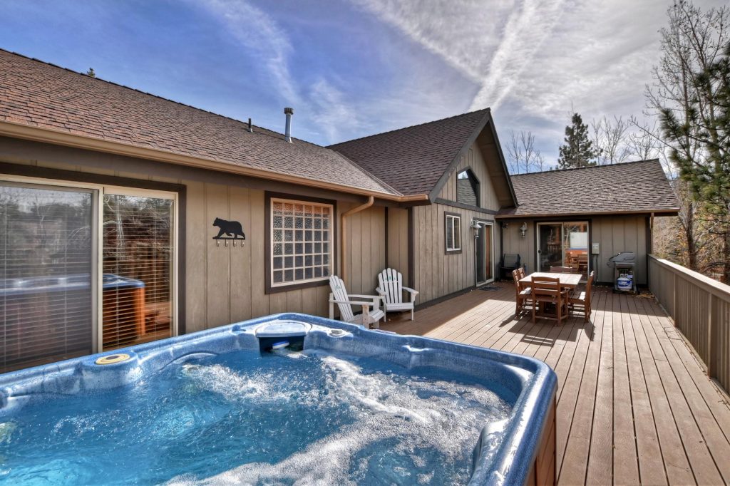Outdoor deck at Copper Moose Lodge in Big Bear featuring a private hot tub, dining area, barbecue grill, and mountain cabin setting.