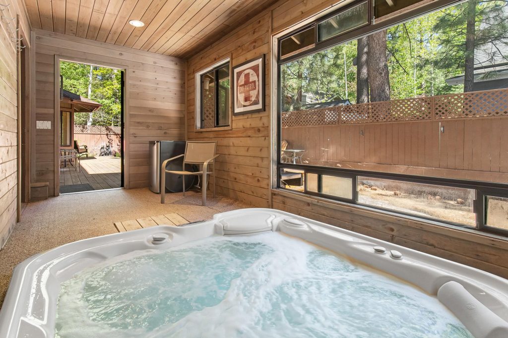 Indoor hot tub area at The Evergreen Lodge with wood panel walls, large windows, and a peaceful forest view in Big Bear Lake, CA