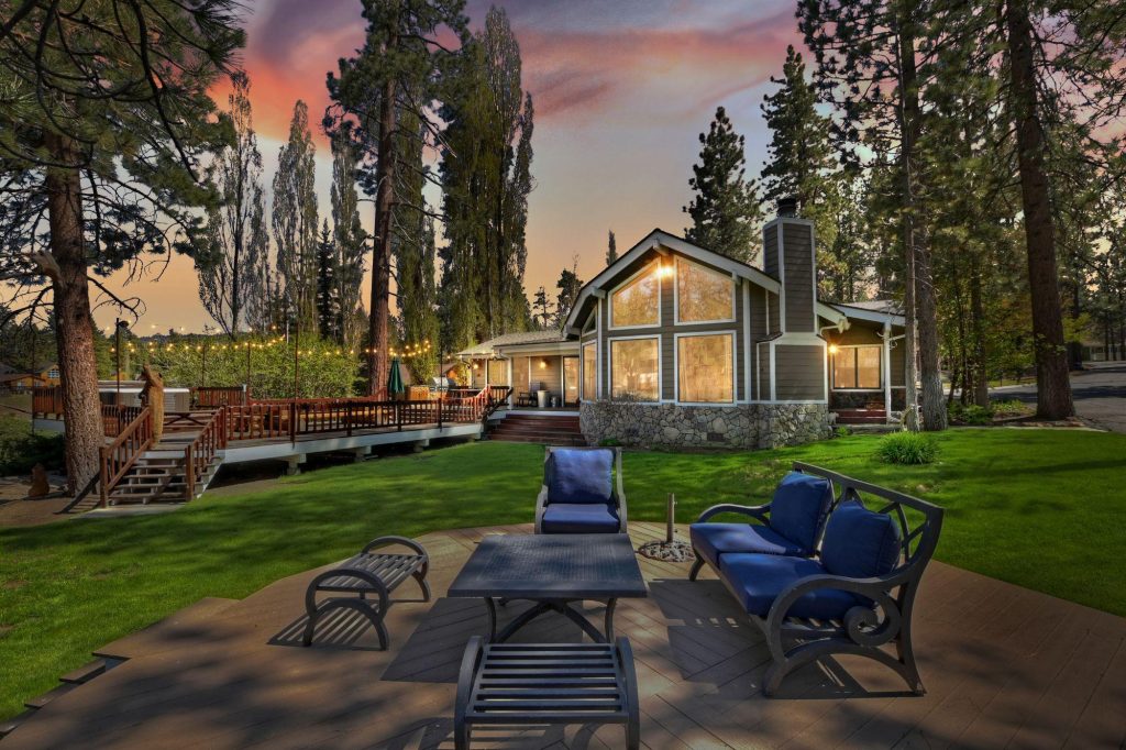 Lakefront house exterior with deck, outdoor seating, and ambient string lights at dusk.