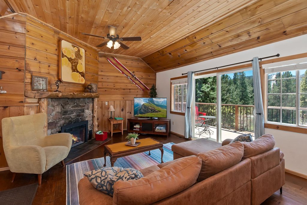 Mountain cabin living room with stone fireplace, wood walls, cozy seating, and forest views