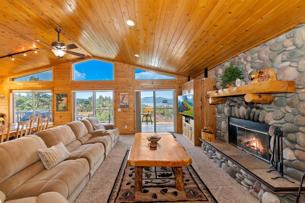 What A View cabin living room with stone fireplace, wood interior, comfortable seating, and scenic lake views