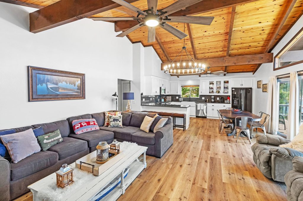 Bright living room and kitchen with vaulted wooden ceiling, cozy sectional sofa, and dining area.