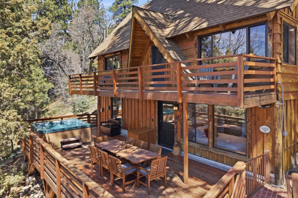 Exterior view of Bear Pines Retreat featuring a spacious wooden deck, outdoor seating area, hot tub, and peaceful forest surroundings