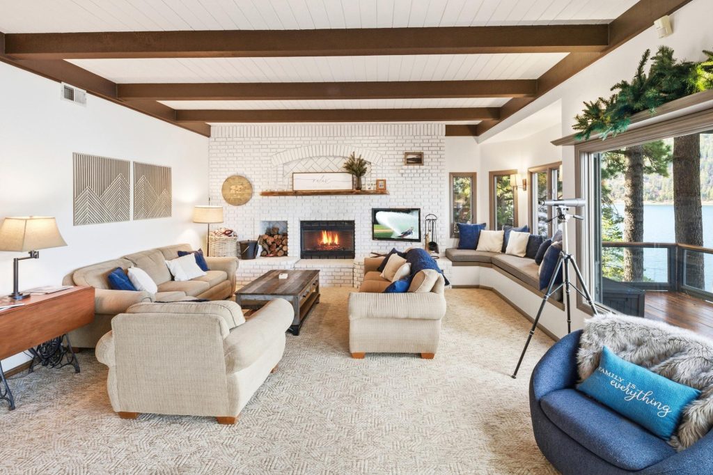 Cozy and bright living room with a lake view, featuring a fireplace, beige sofas, and a built-in window seating area.