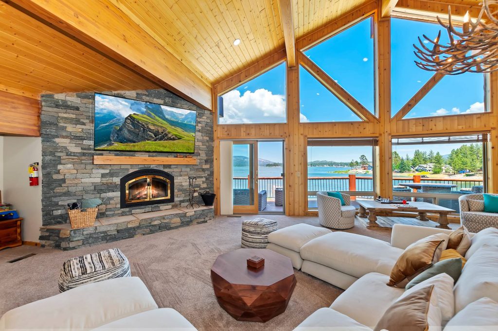 Spacious lakefront cabin living room with fireplace, large windows, and scenic lake views