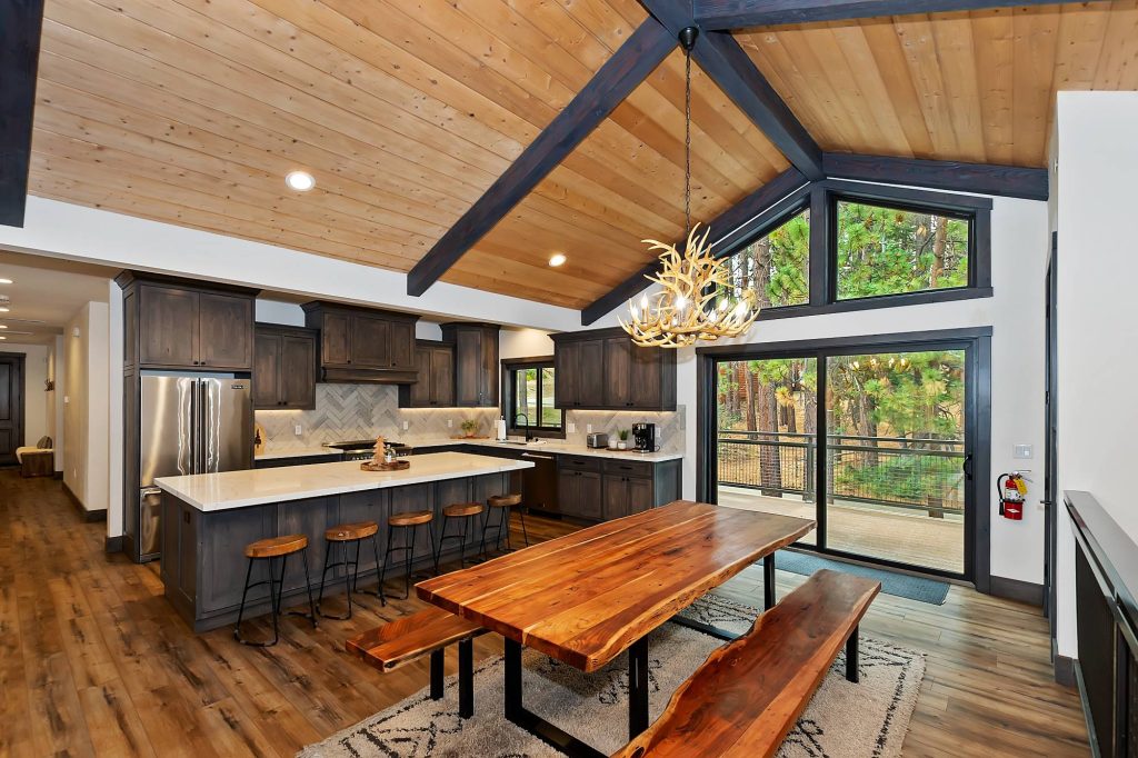 Modern cabin kitchen and dining area at Living The Dream with wood ceilings, island counter, and forest views