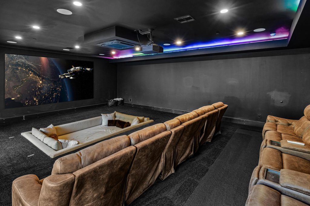 A home theater room in Big Bear with a large screen, two rows of plush seating, and a color-changing light strip on the ceiling.