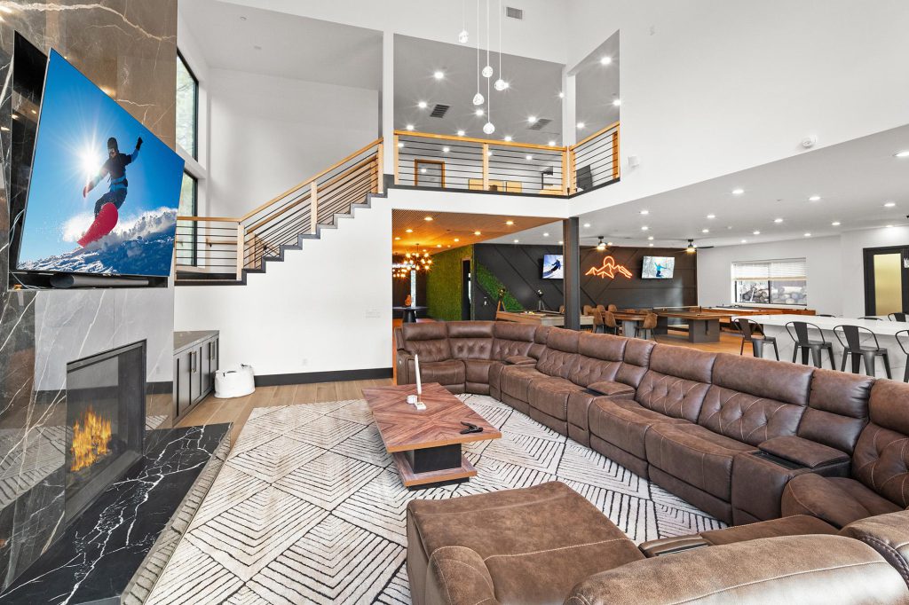 A modern cabin living room in Big Bear with a large brown sectional sofa, a marble fireplace, and an open view of a game area with a pool table.