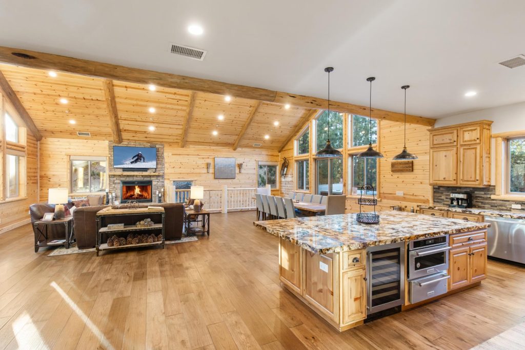 Spacious Luna Lodge interior with wood ceilings, stone fireplace, modern kitchen island, dining area, and cozy living space in Big Bear Lake, CA