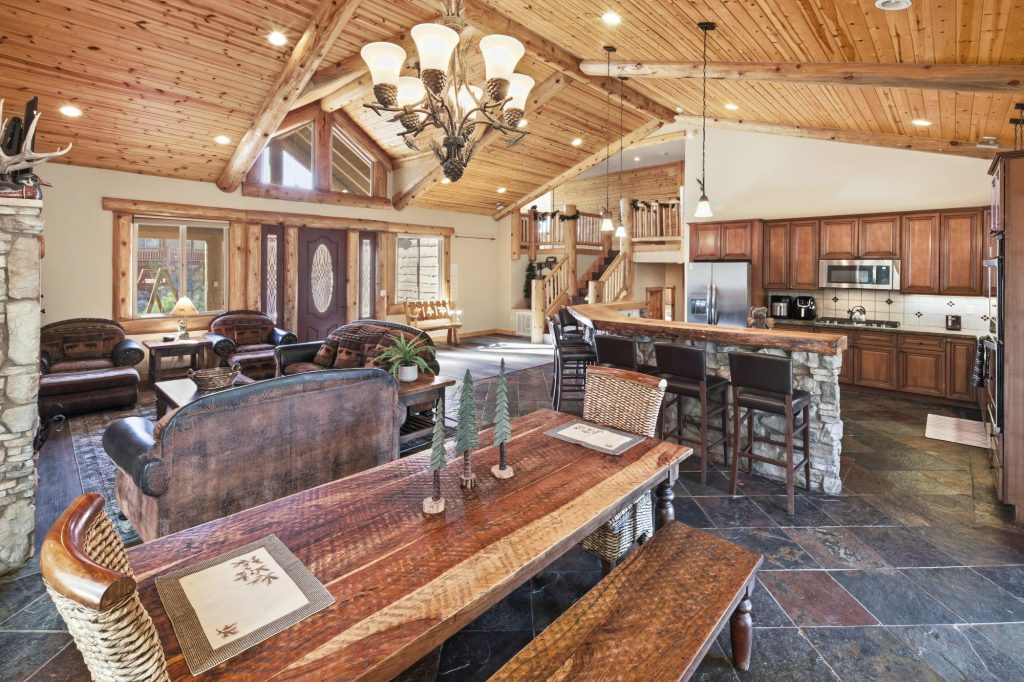 Spacious interior of Castle Glen Lodge featuring vaulted wood ceilings, a rustic dining area, stone breakfast bar, gourmet kitchen, and cozy living room seating.