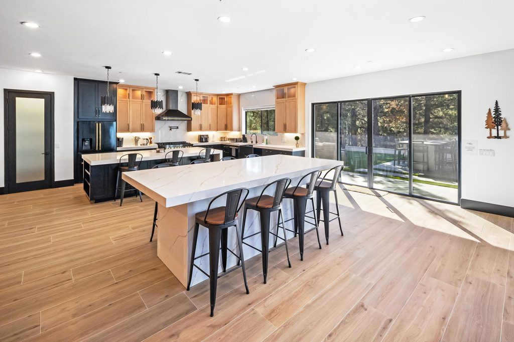 A modern kitchen with a large white island, black bar stools, and sliding glass doors leading to a backyard in Big Bear.
