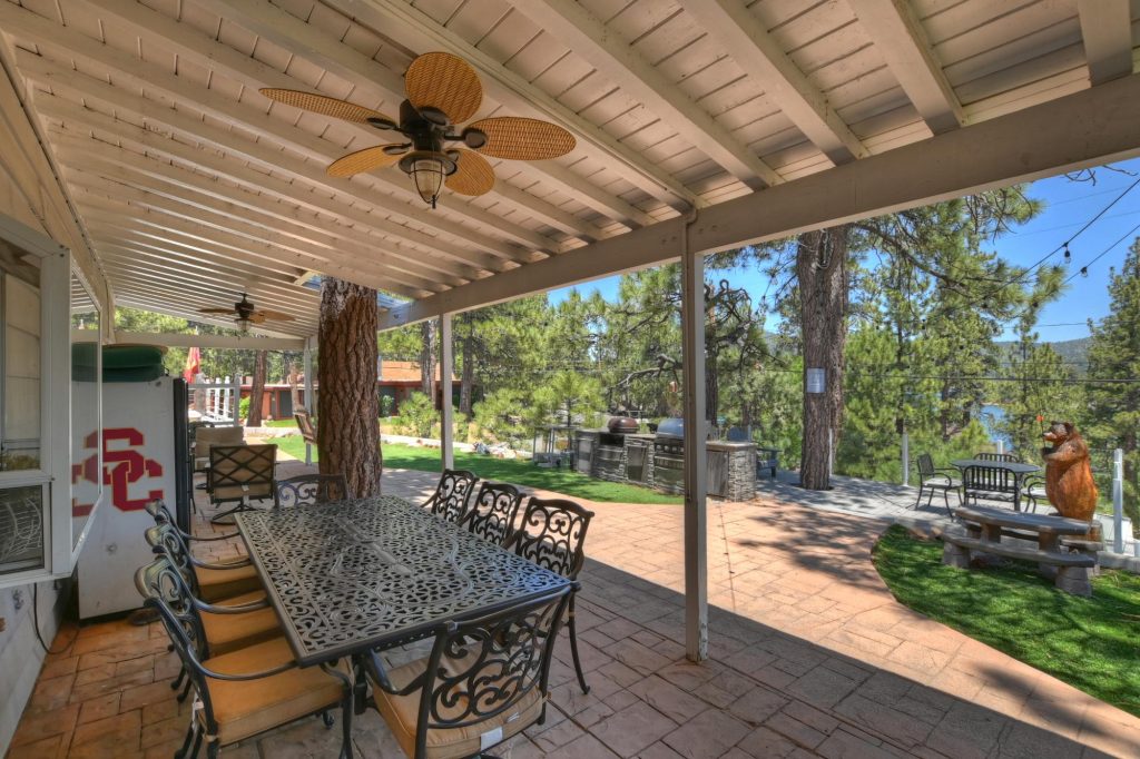 Outdoor patio at Ponderosa by the Lake cabin featuring seating area, BBQ grill, pine trees, and lake views in Big Bear Lake, CA