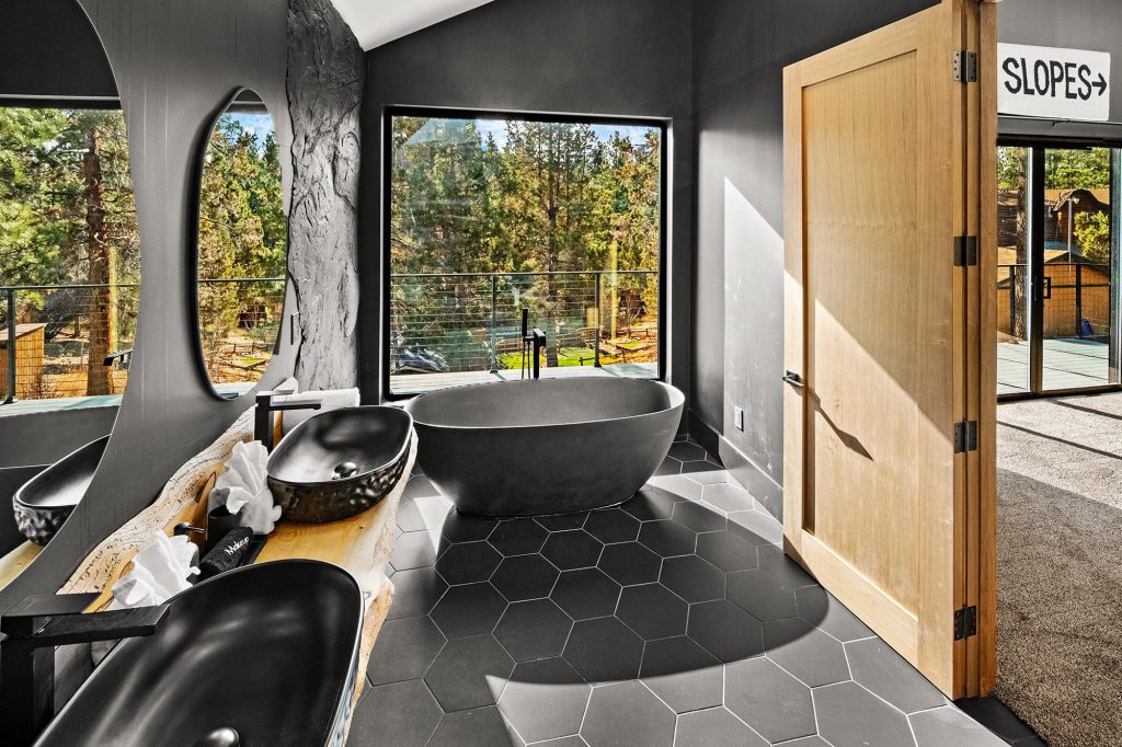 A modern bathroom at Big Bear with a standalone tub, unique sinks, and large windows looking out to trees.