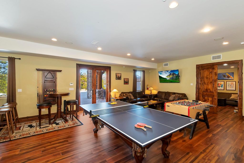 Spacious game room with ping pong table, foosball, pool table, leather couches, and wall-mounted TV, with doors leading to an outdoor area.