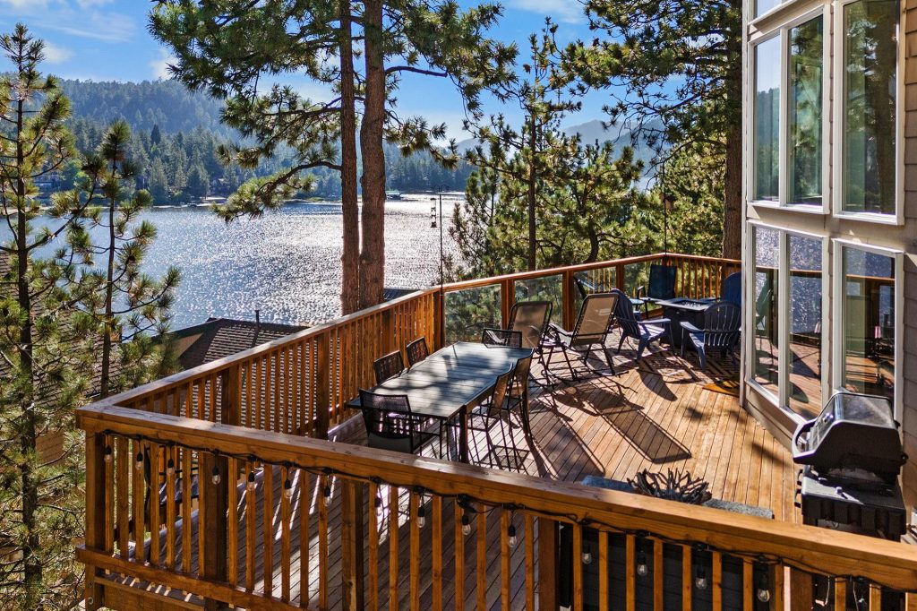 Lakefront deck at Window Wonderland cabin featuring outdoor seating, BBQ grill, pine trees, and scenic Big Bear Lake views